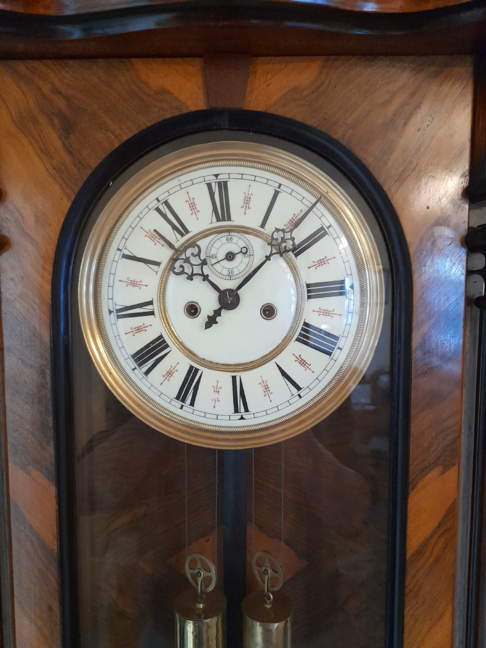 A dark walnut-cased Gustav Becker twin-weight Vienna regulator wall clock featuring turned side columns, carved cresting, twin brass weights, and a white enamel Roman numeral dial. View II