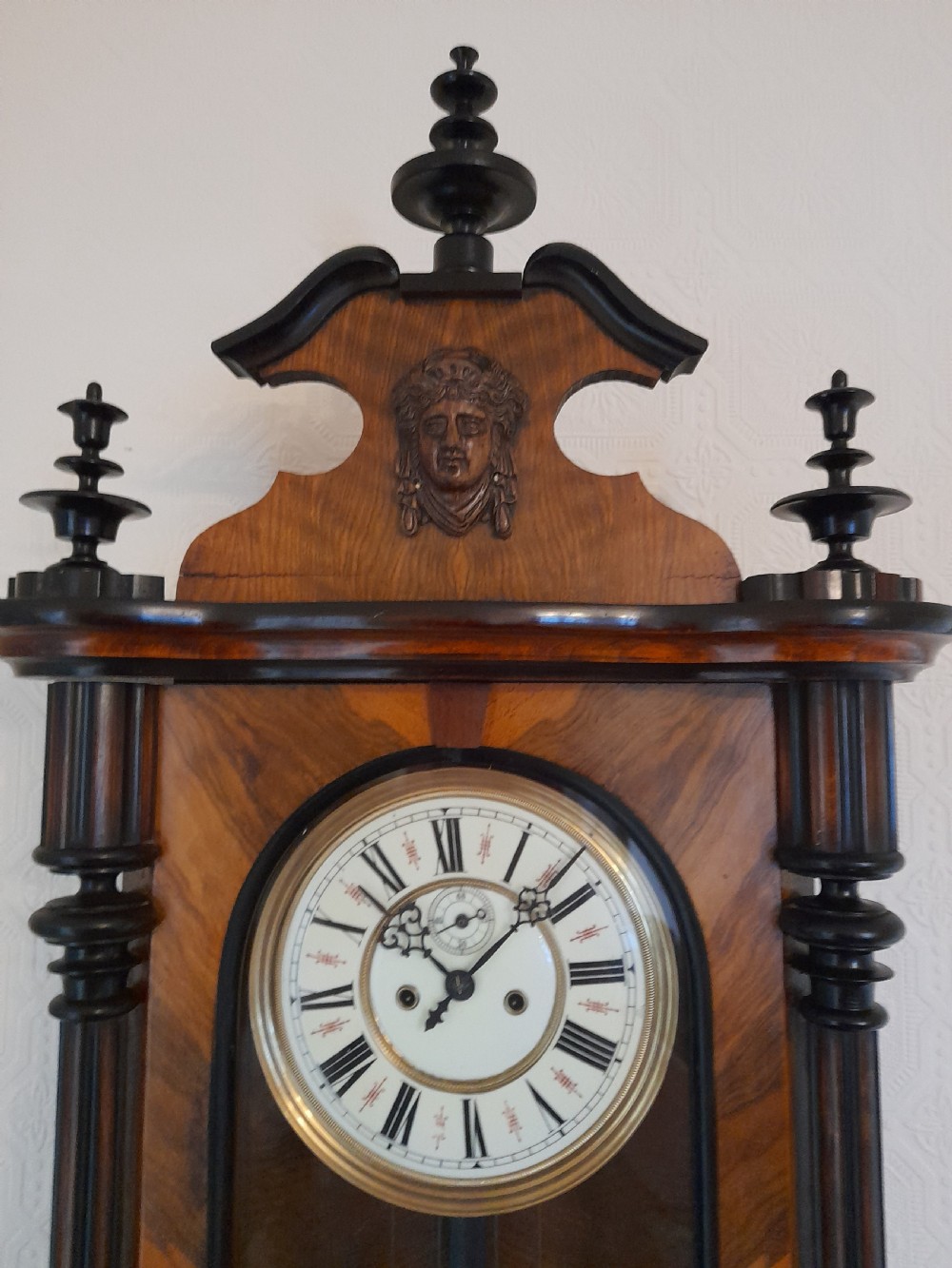 A dark walnut-cased Gustav Becker twin-weight Vienna regulator wall clock featuring turned side columns, carved cresting, twin brass weights, and a white enamel Roman numeral dial. View III