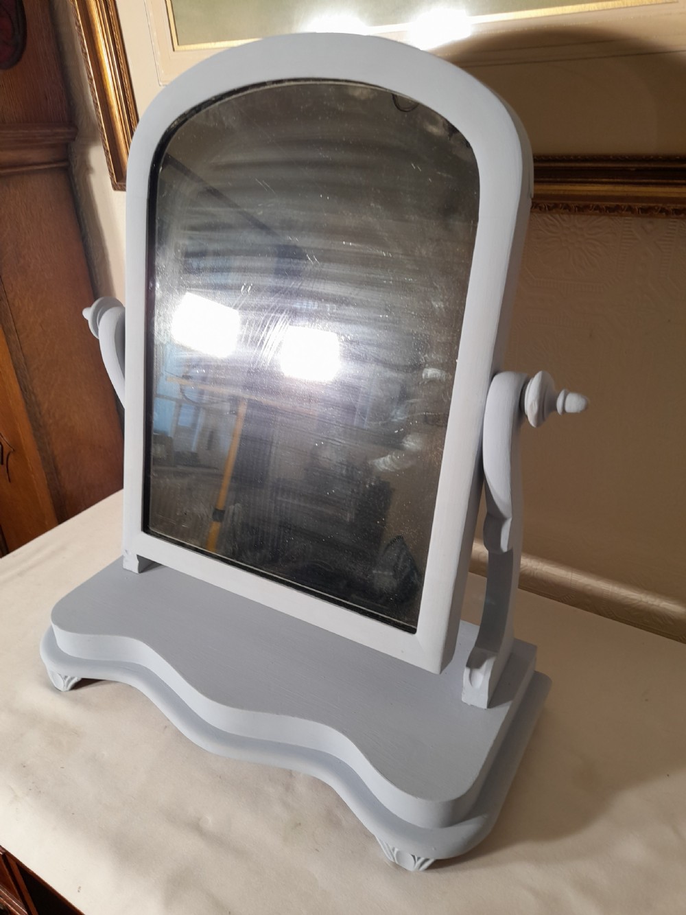 A grey-painted Victorian swing dressing table mirror featuring an arched glass frame set between turned supports on a contoured serpentine base.