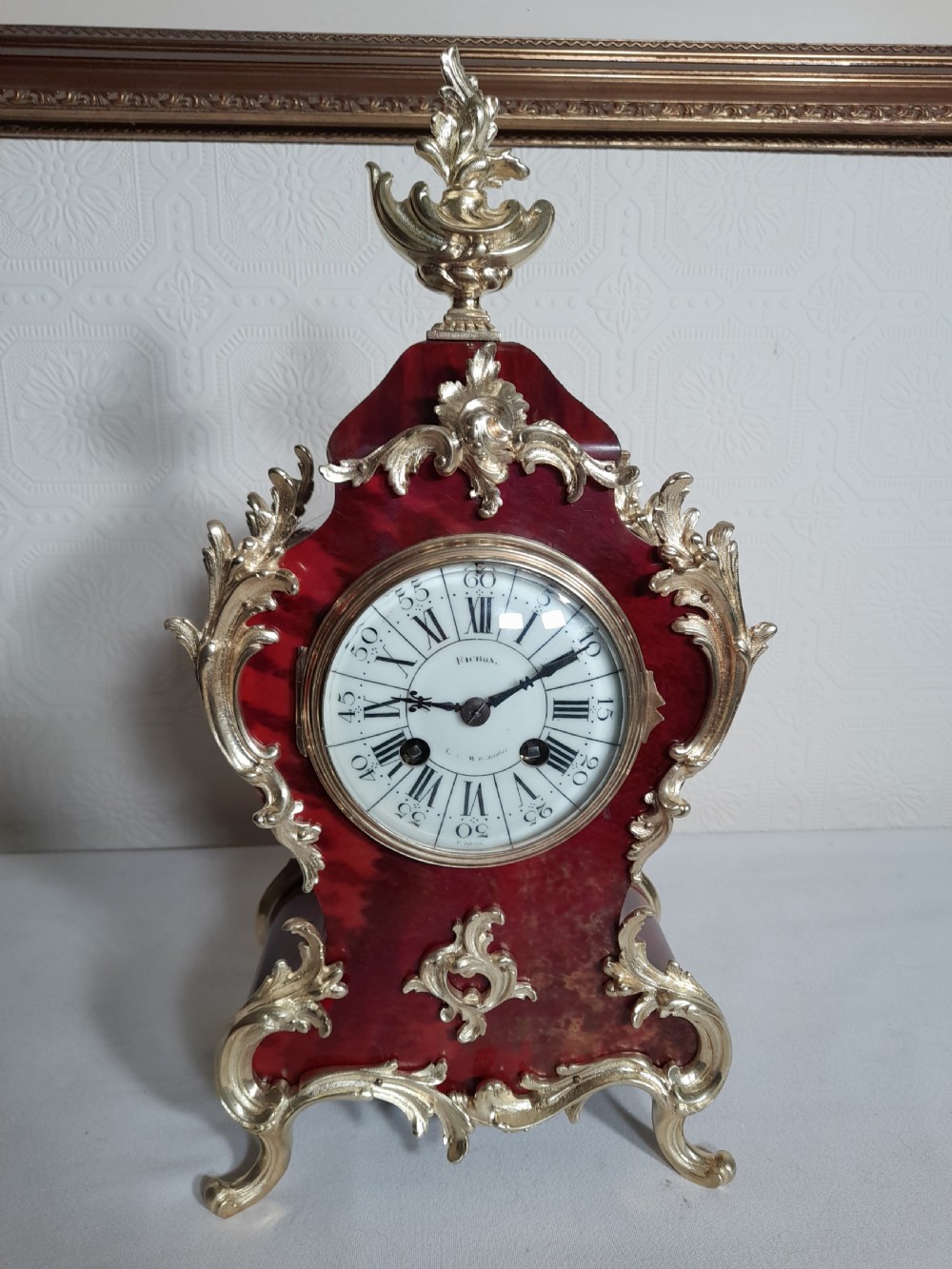 A French Rococo Revival style mantel clock featuring crimson tortoiseshell veneering, ornate gilt bronze mounts, and a white enamel dial with Roman numerals.