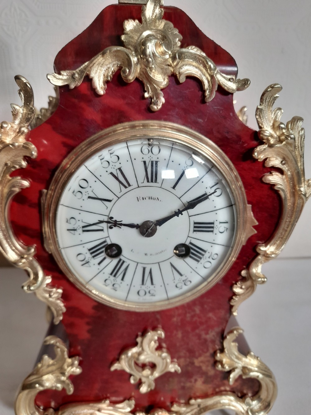 A French Rococo Revival style mantel clock featuring crimson tortoiseshell veneering, ornate gilt bronze mounts, and a white enamel dial with Roman numerals. View II