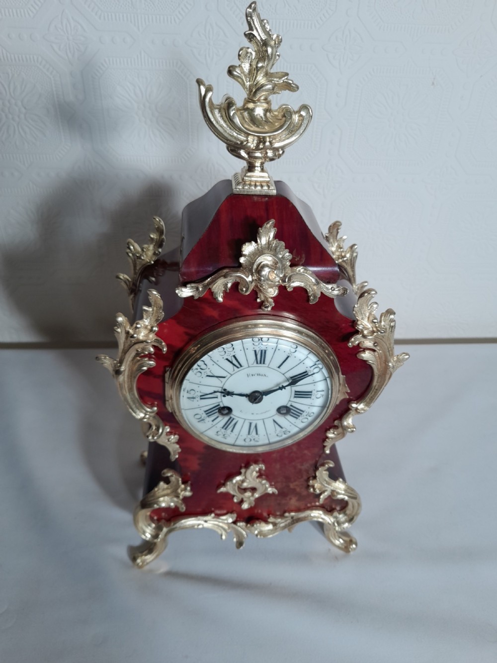 A French Rococo Revival style mantel clock featuring crimson tortoiseshell veneering, ornate gilt bronze mounts, and a white enamel dial with Roman numerals. View VI