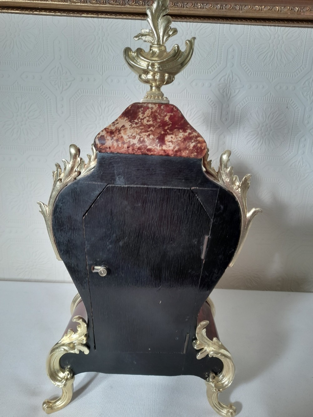 A French Rococo Revival style mantel clock featuring crimson tortoiseshell veneering, ornate gilt bronze mounts, and a white enamel dial with Roman numerals. View VII