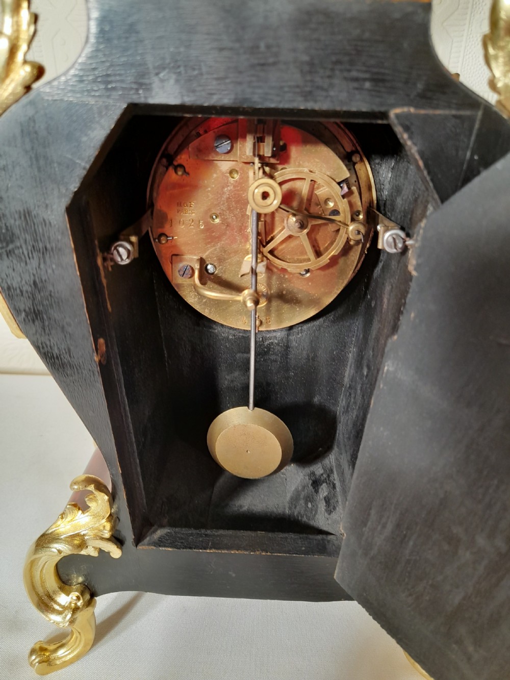 A French Rococo Revival style mantel clock featuring crimson tortoiseshell veneering, ornate gilt bronze mounts, and a white enamel dial with Roman numerals. View VIII
