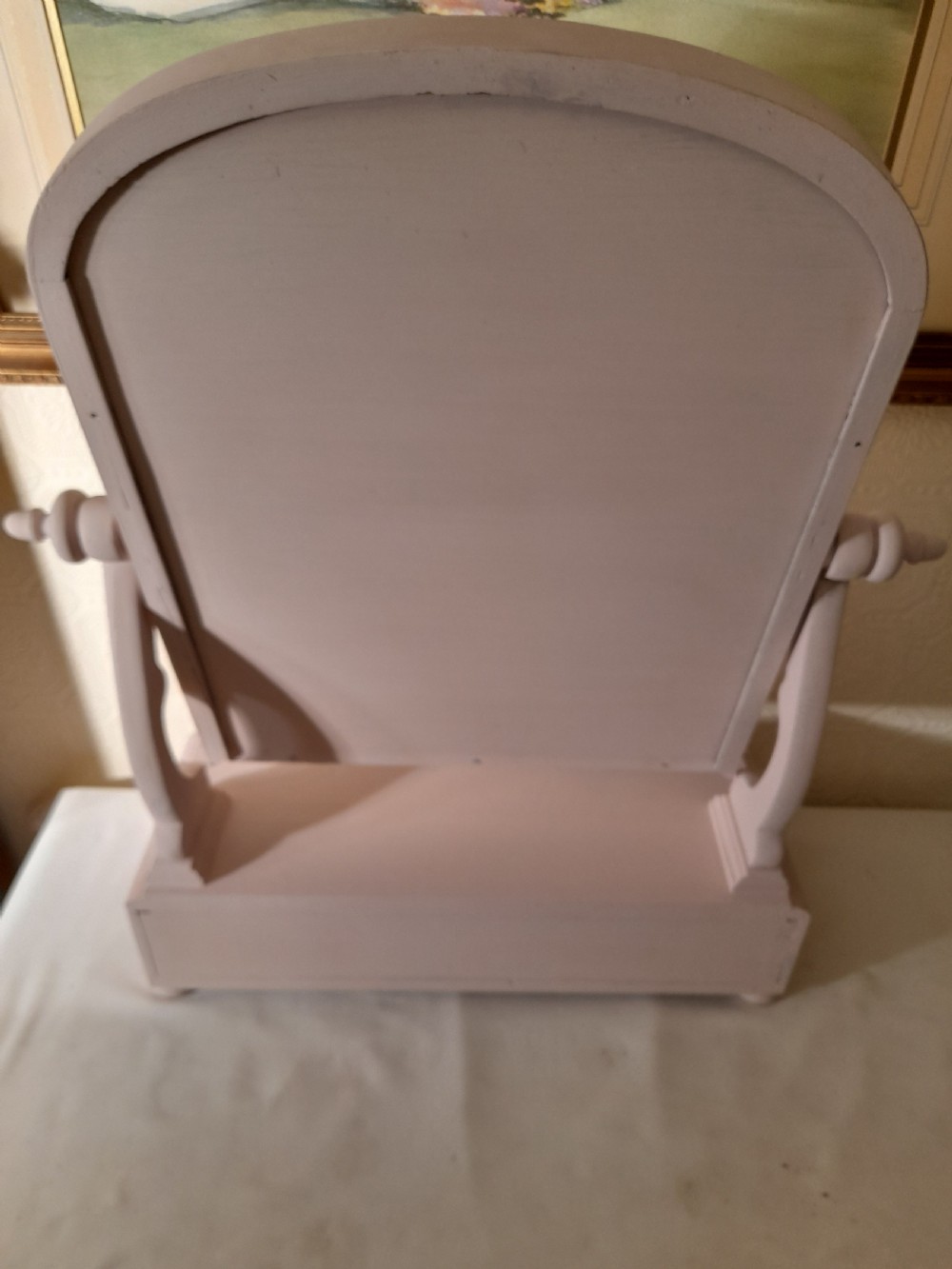 A pale pink painted wooden dressing table mirror featuring an arched tilting glass frame, side turned support pins, and a single drawer in the base plinth. View IV