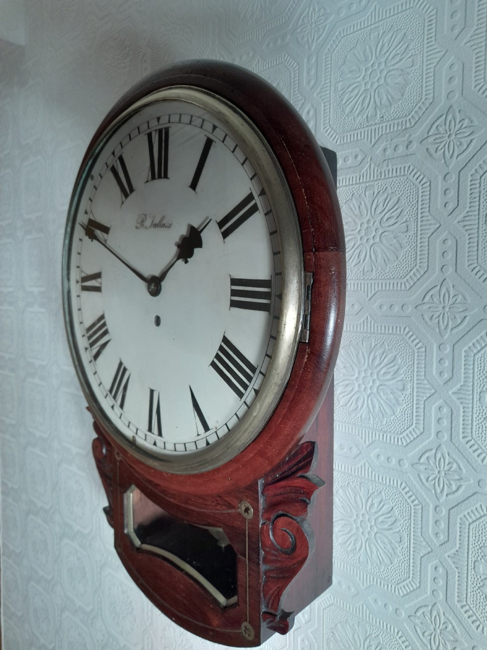 A Victorian rosewood drop-dial wall clock with Roman numerals on a white face, brass accents, and a lower glazed pendulum window. View II