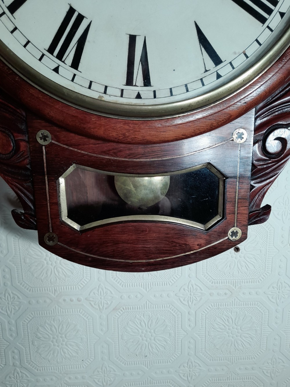 A Victorian rosewood drop-dial wall clock with Roman numerals on a white face, brass accents, and a lower glazed pendulum window. View III