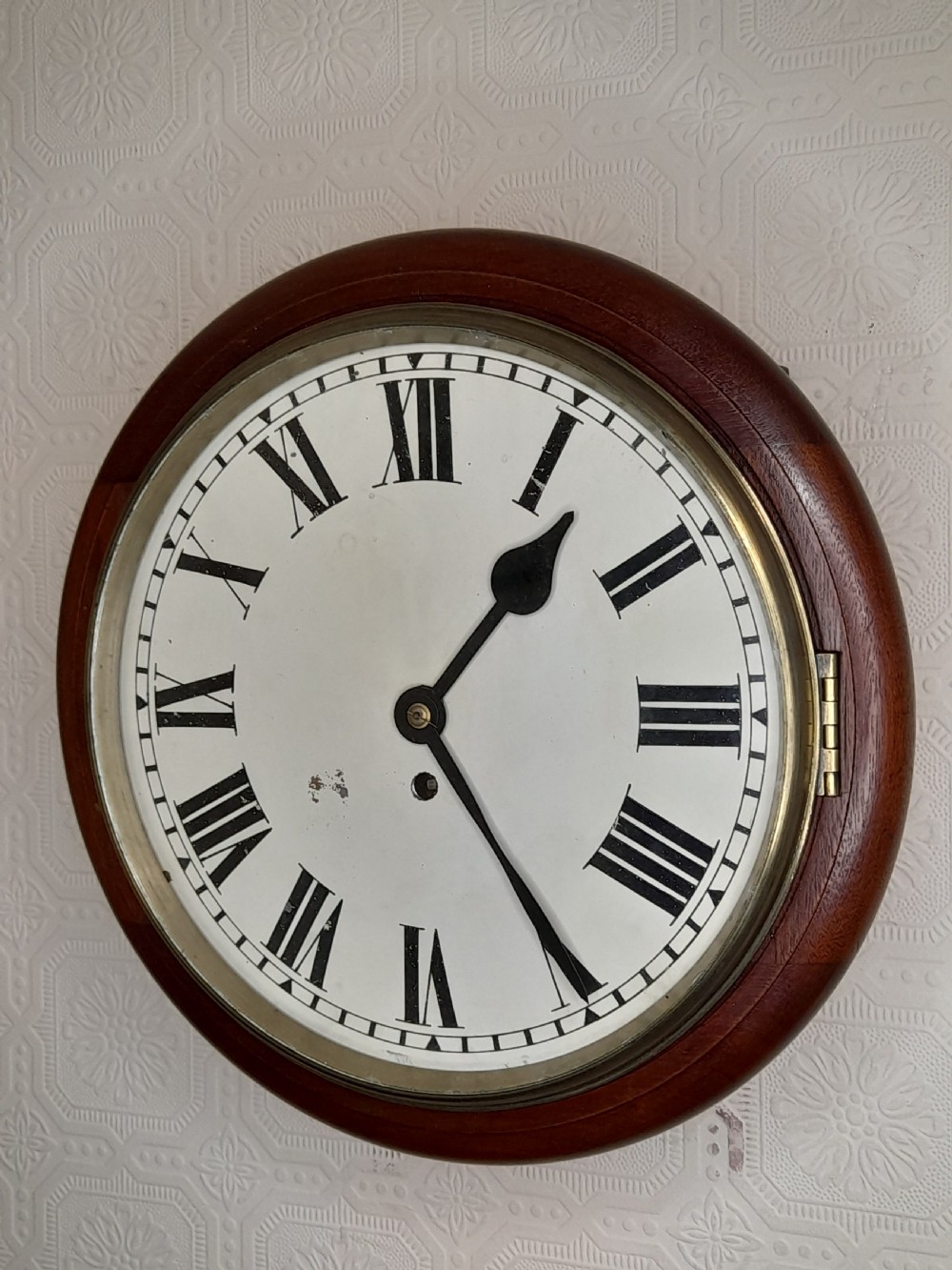 A circular mahogany fusee wall clock featuring a white painted dial with black Roman numerals, black hands, and a hinged brass bezel.