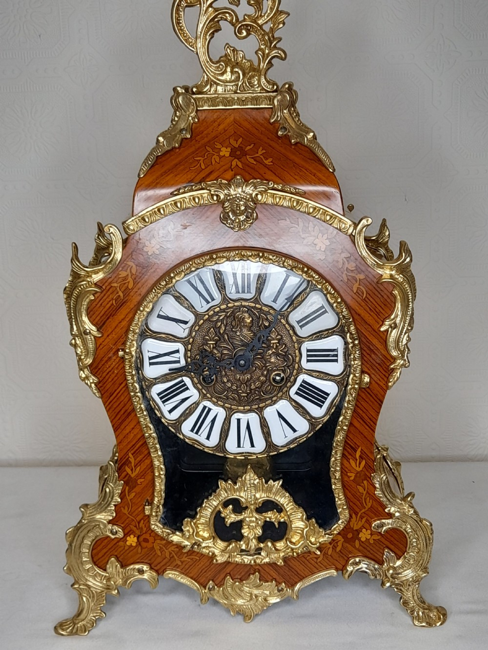 A Louis XIV style bracket clock featuring floral wood marquetry, ornate gilt-bronze mounts, and a dial with white enamel Roman numeral cartouches.