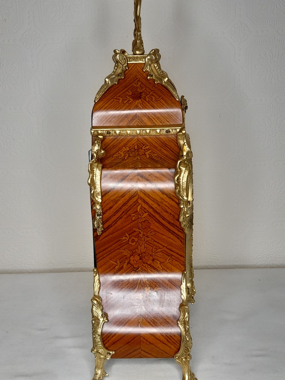 A Louis XIV style bracket clock featuring floral wood marquetry, ornate gilt-bronze mounts, and a dial with white enamel Roman numeral cartouches. View II