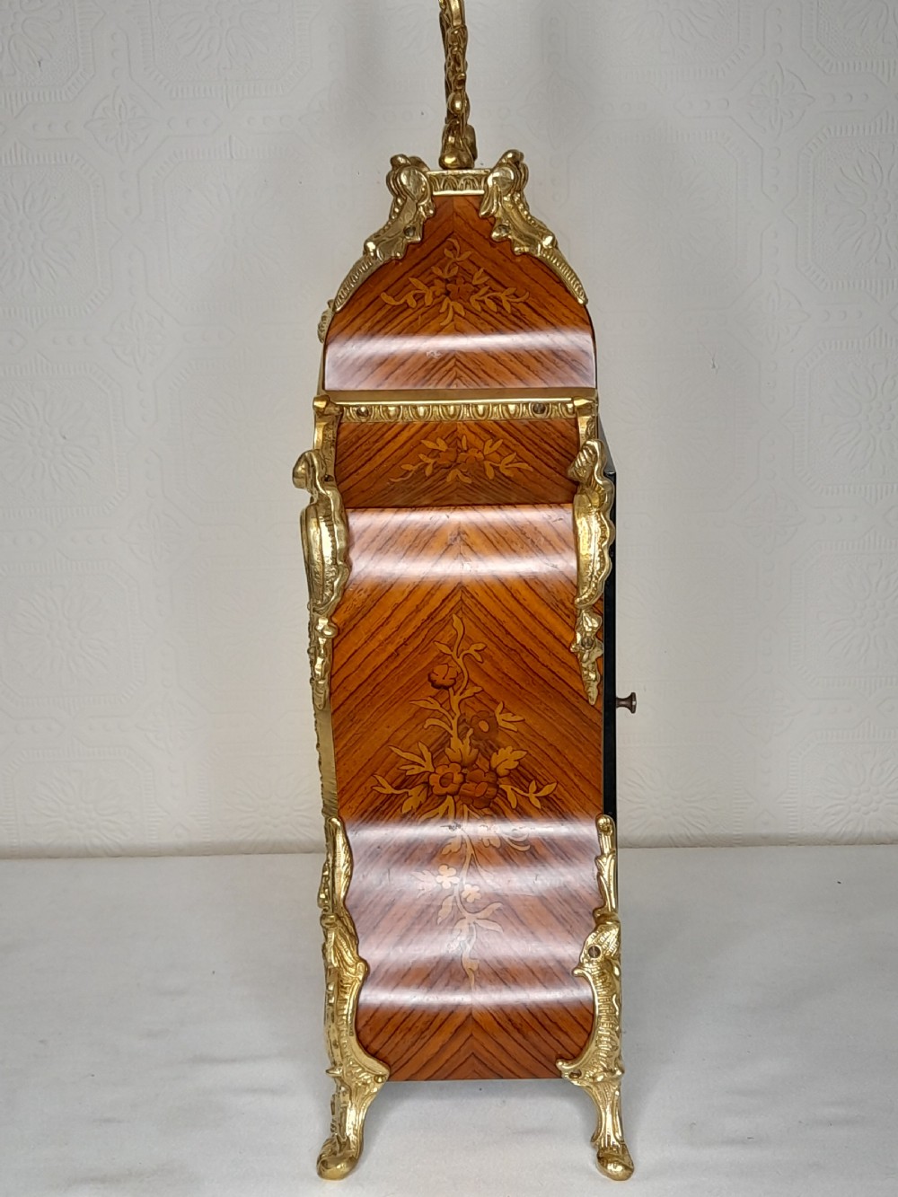 A Louis XIV style bracket clock featuring floral wood marquetry, ornate gilt-bronze mounts, and a dial with white enamel Roman numeral cartouches. View III