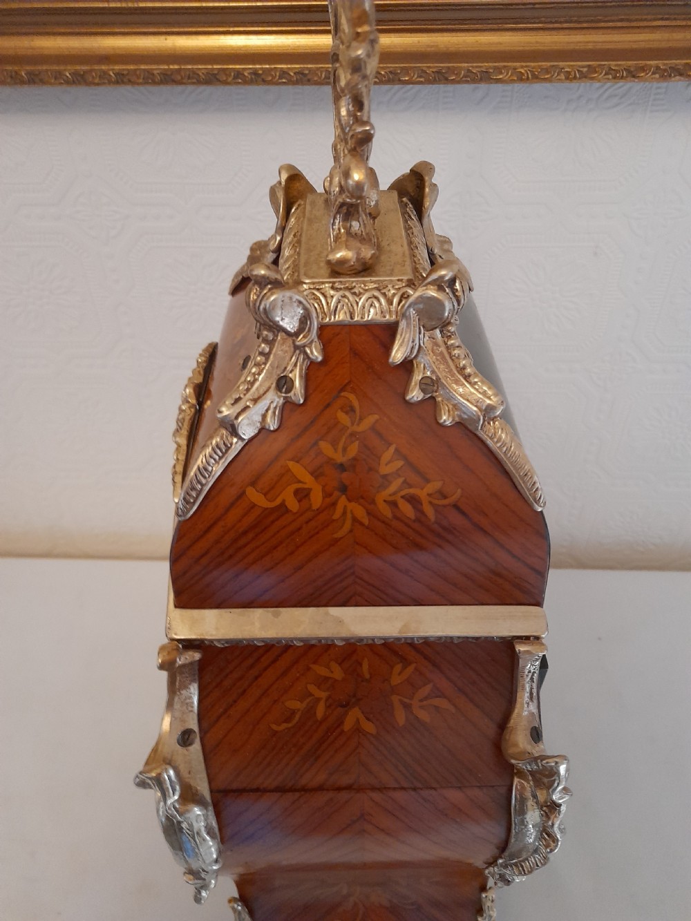 A Louis XIV style bracket clock featuring floral wood marquetry, ornate gilt-bronze mounts, and a dial with white enamel Roman numeral cartouches. View VII