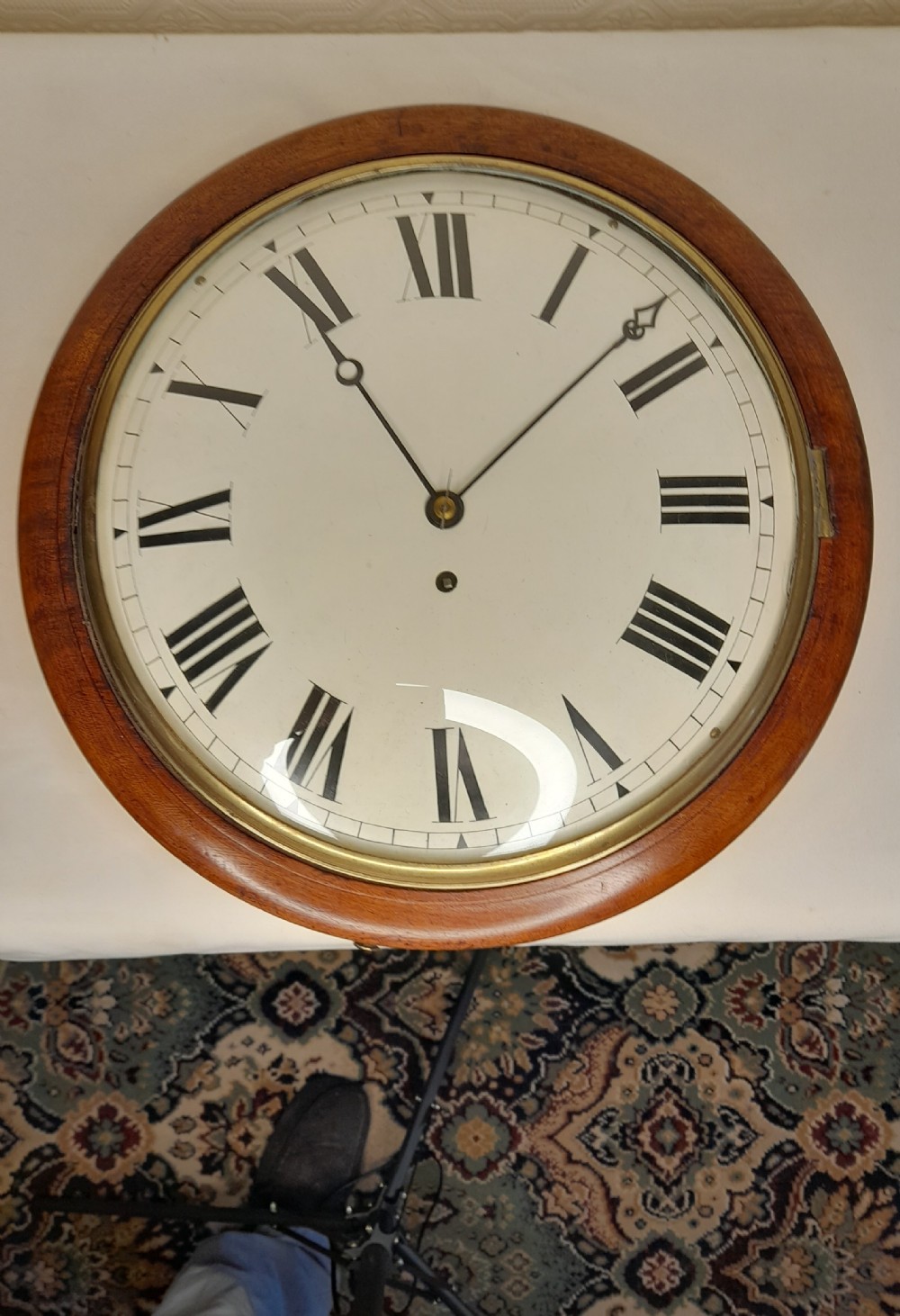 An antique circular mahogany wall clock featuring a cream convex dial with black Roman numerals and a polished brass bezel.