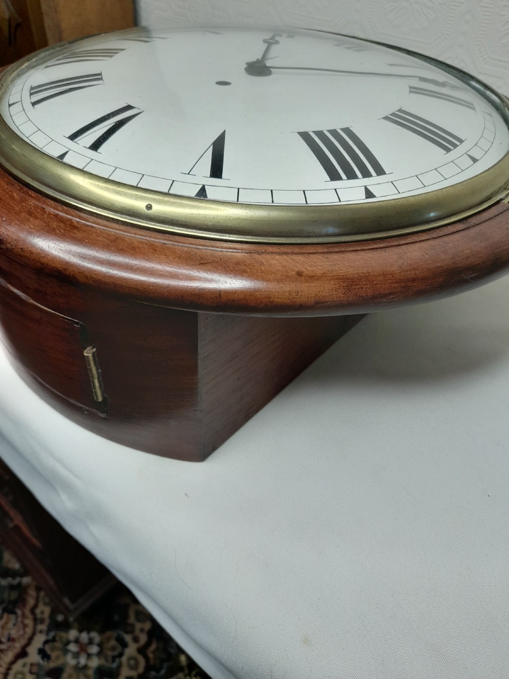 An antique circular mahogany wall clock featuring a cream convex dial with black Roman numerals and a polished brass bezel. View II