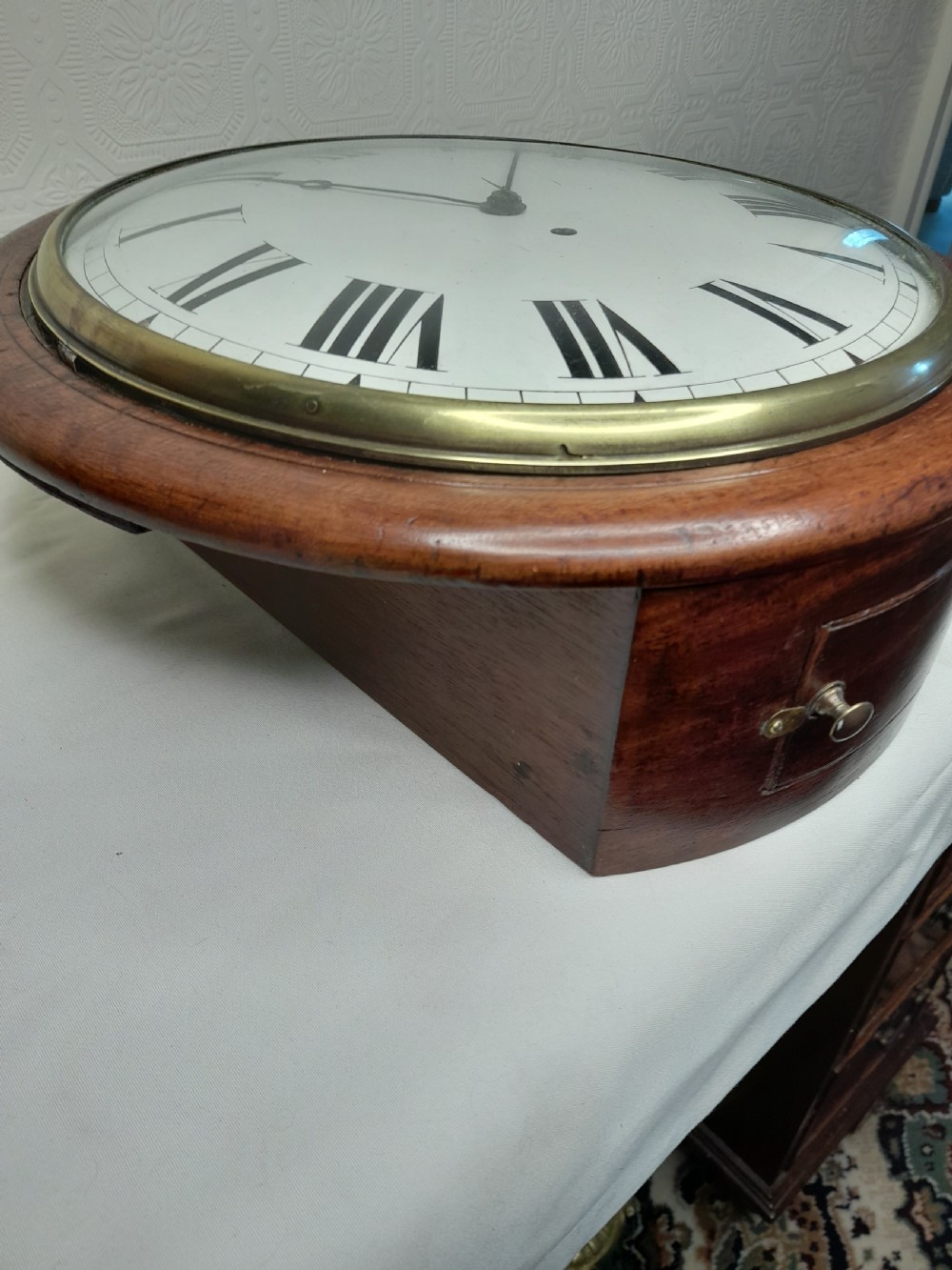 An antique circular mahogany wall clock featuring a cream convex dial with black Roman numerals and a polished brass bezel. View III