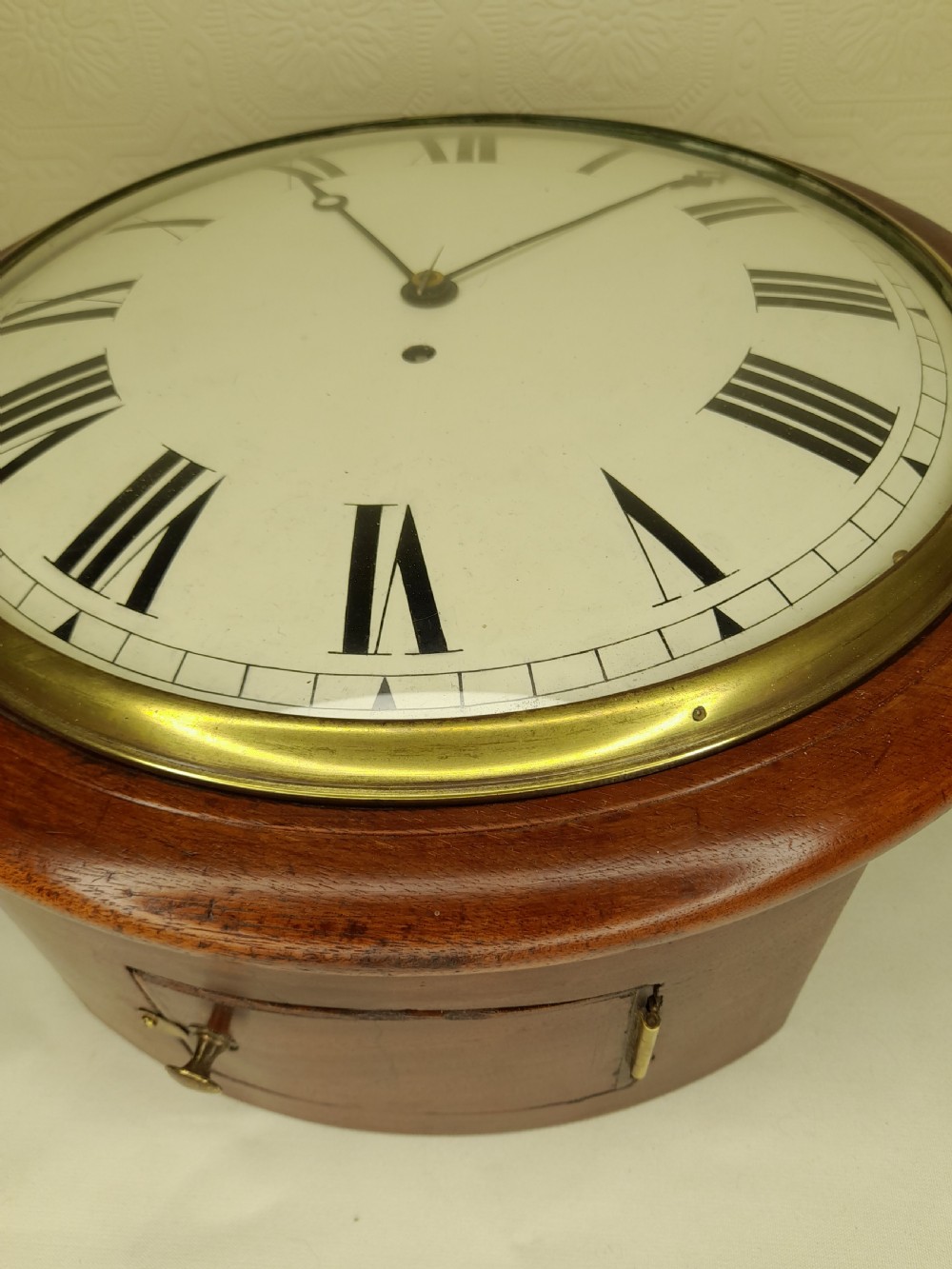 An antique circular mahogany wall clock featuring a cream convex dial with black Roman numerals and a polished brass bezel. View IV