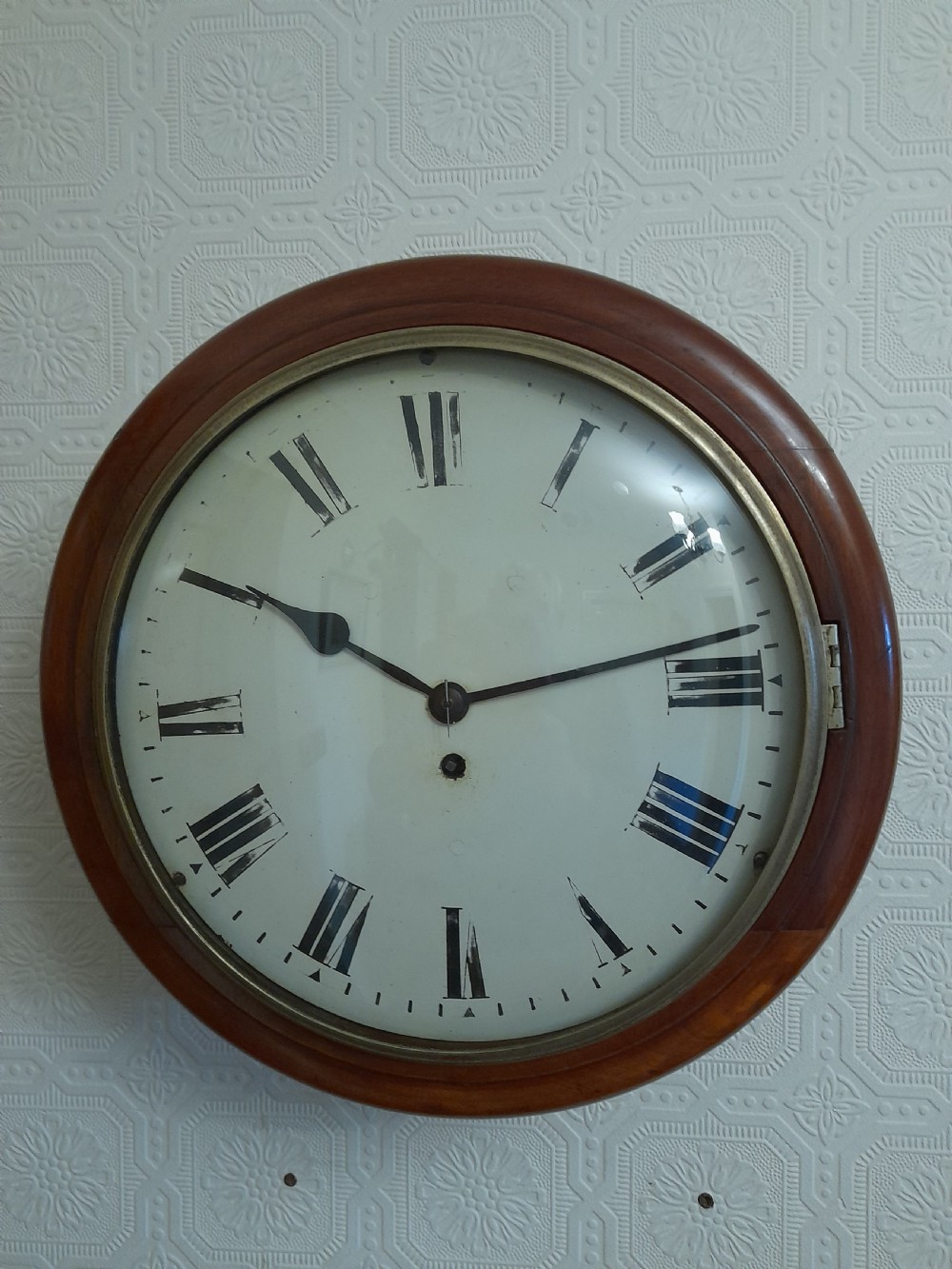 A circular Victorian wall clock featuring a turned mahogany wooden case, a brass glass bezel, and a white dial with black Roman numerals.