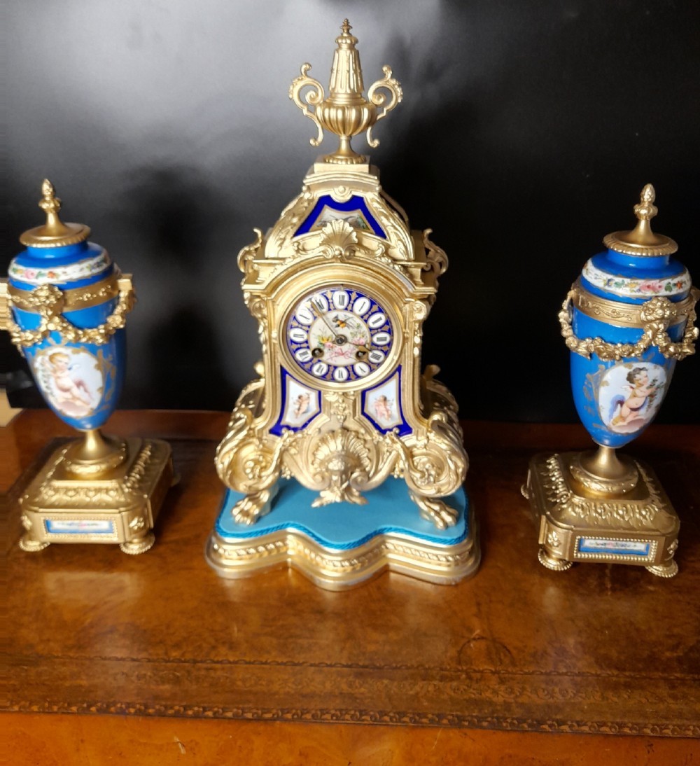 A French gilt bronze clock garniture featuring a central mantel clock with hand-painted blue porcelain panels flanked by two matching ornamental urns.
