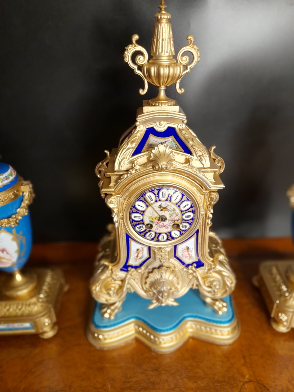 A French gilt bronze clock garniture featuring a central mantel clock with hand-painted blue porcelain panels flanked by two matching ornamental urns. View III