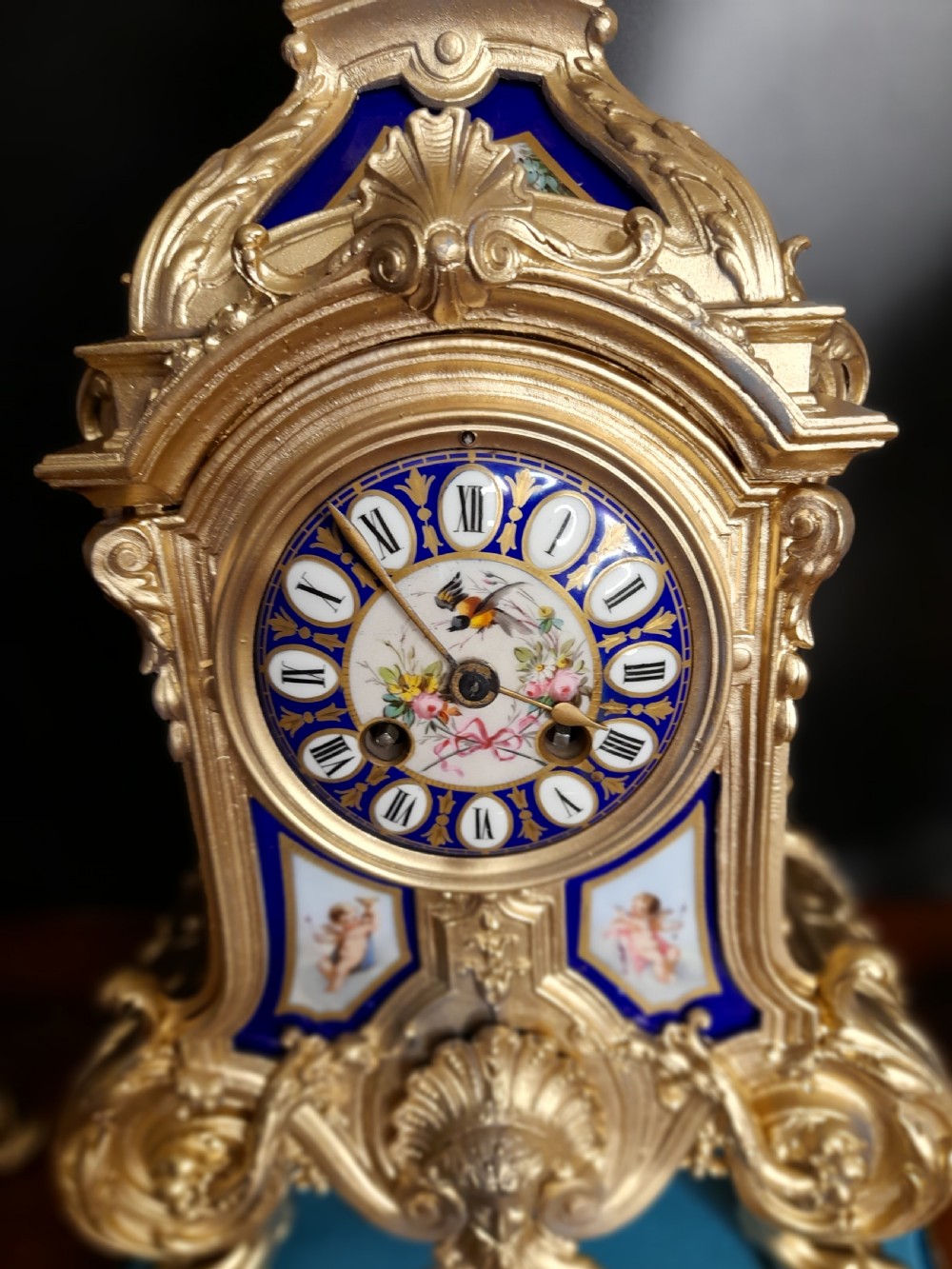 A French gilt bronze clock garniture featuring a central mantel clock with hand-painted blue porcelain panels flanked by two matching ornamental urns. View V