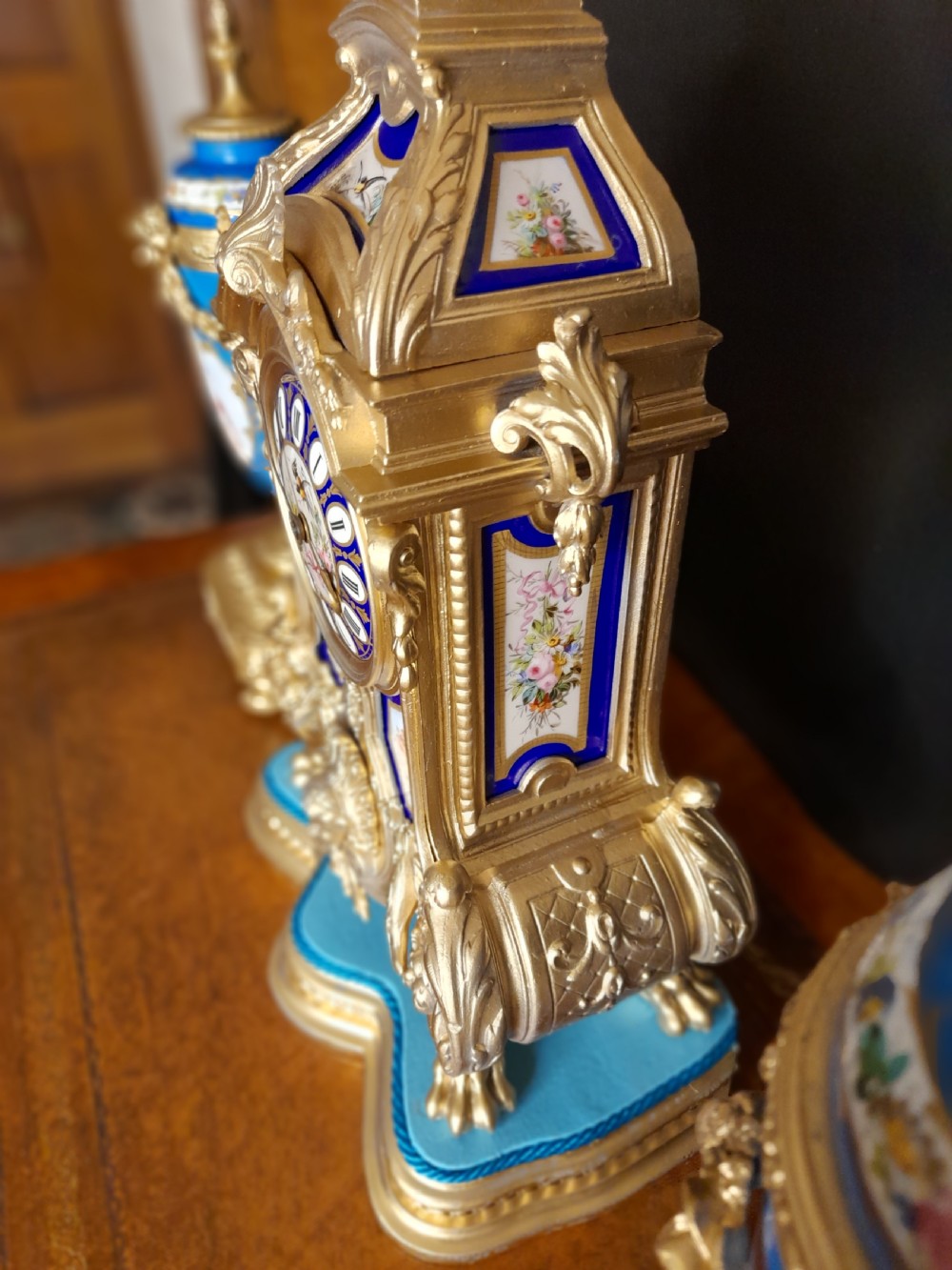 A French gilt bronze clock garniture featuring a central mantel clock with hand-painted blue porcelain panels flanked by two matching ornamental urns. View VII