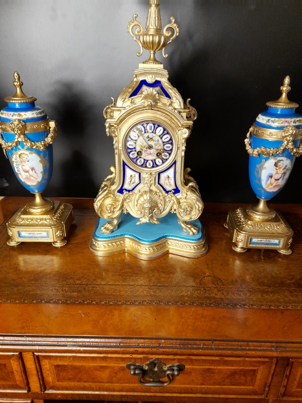 A French gilt bronze clock garniture featuring a central mantel clock with hand-painted blue porcelain panels flanked by two matching ornamental urns. View XII