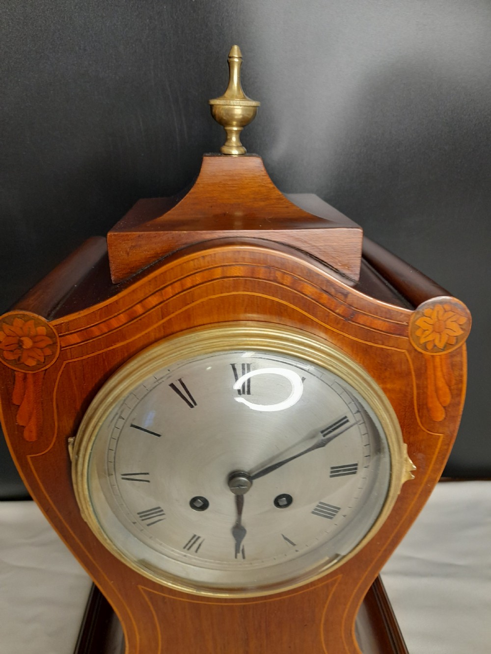 An Art Nouveau satinwood mantel clock featuring floral marquetry inlays, a silvered Roman numeral dial, a brass finial, and brass bracket feet. View II