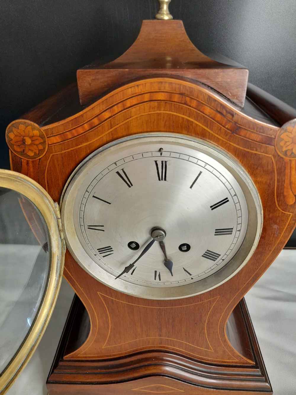 An Art Nouveau satinwood mantel clock featuring floral marquetry inlays, a silvered Roman numeral dial, a brass finial, and brass bracket feet. View III