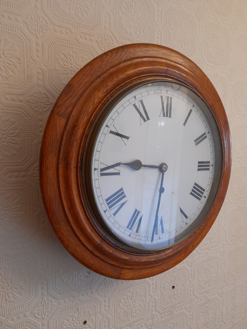 A circular antique golden oak wall clock featuring a white dial with black Roman numerals and a brass-rimmed glass cover. View II