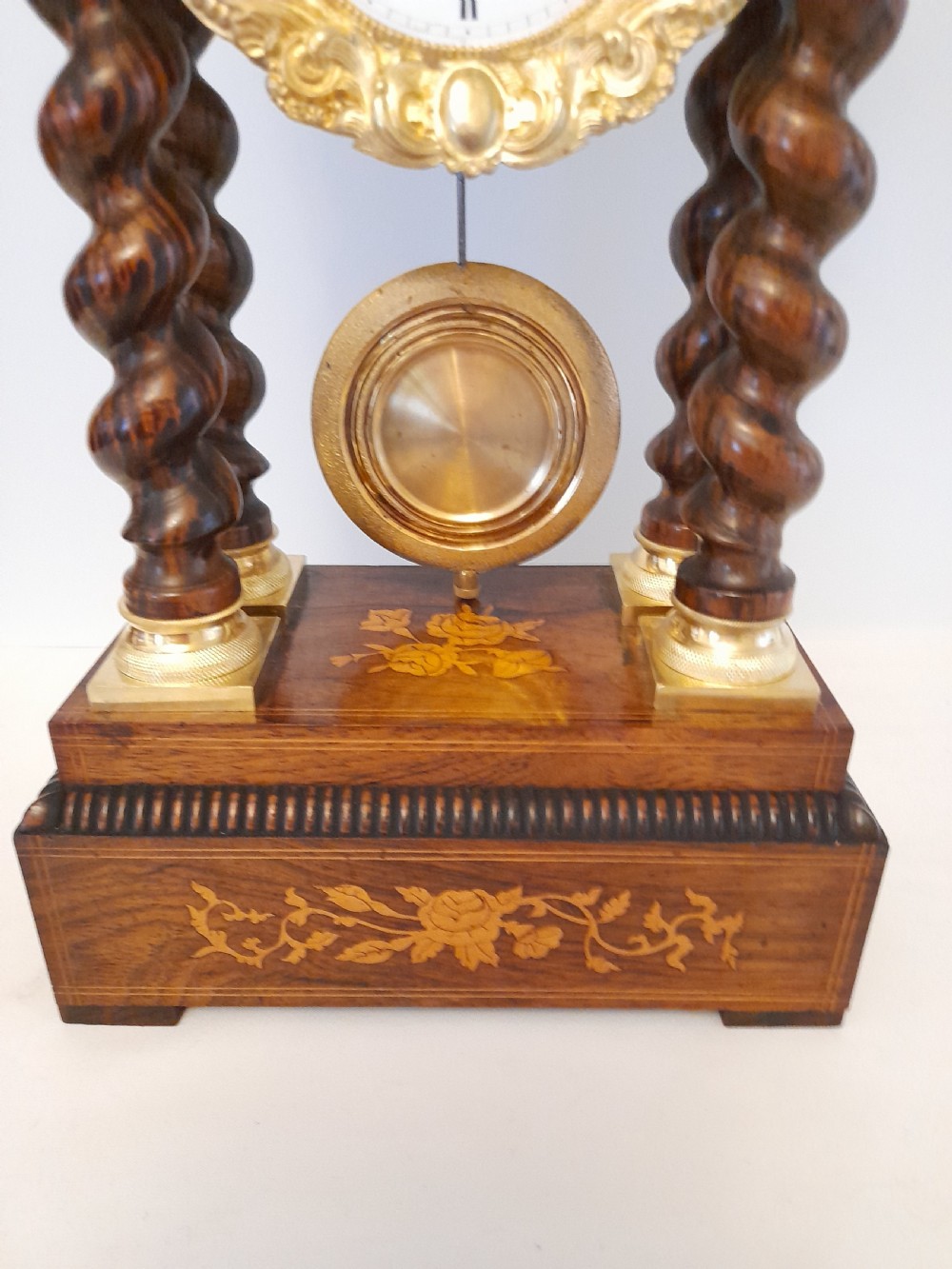 A 19th-century French rosewood portico clock featuring twisted columns, floral marquetry inlays, a white enamel dial with Roman numerals, and a gilt metal pendulum. View III