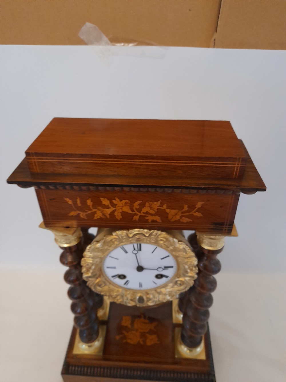A 19th-century French rosewood portico clock featuring twisted columns, floral marquetry inlays, a white enamel dial with Roman numerals, and a gilt metal pendulum. View VII