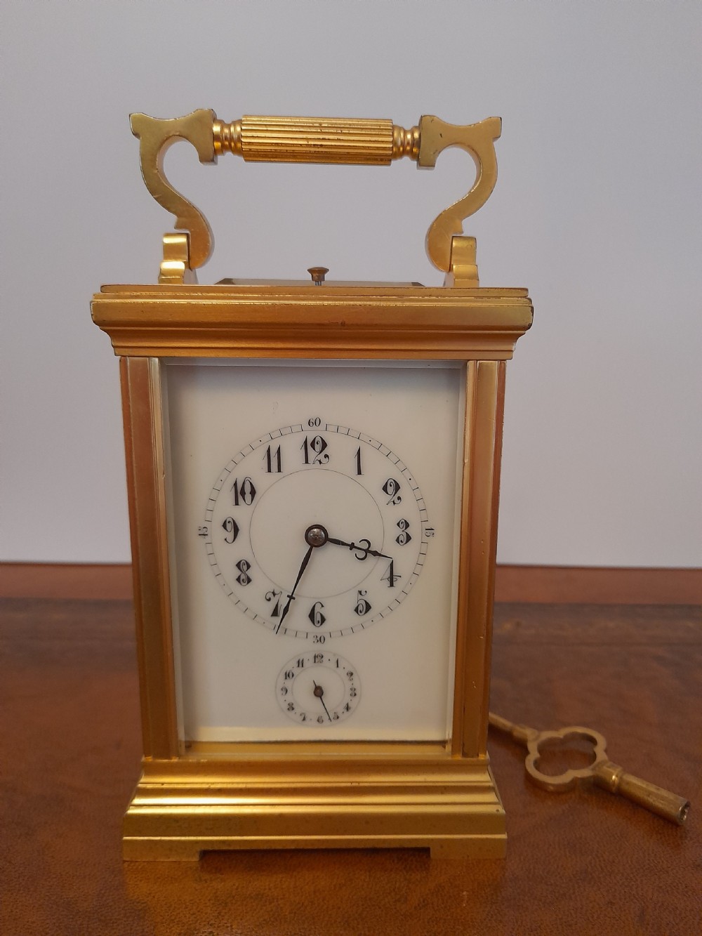 A gilt brass carriage clock featuring a fluted top handle, bevelled glass panels, a white enamel main dial with Arabic numerals, an alarm sub-dial, and an accompanying winding key.