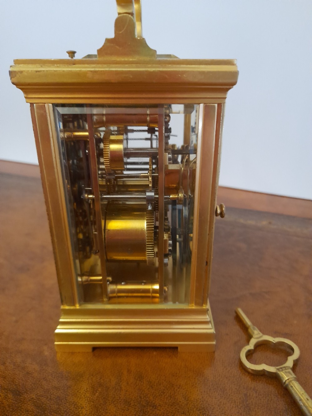 A gilt brass carriage clock featuring a fluted top handle, bevelled glass panels, a white enamel main dial with Arabic numerals, an alarm sub-dial, and an accompanying winding key. View IV