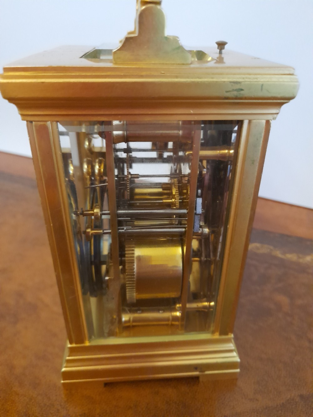 A gilt brass carriage clock featuring a fluted top handle, bevelled glass panels, a white enamel main dial with Arabic numerals, an alarm sub-dial, and an accompanying winding key. View VI