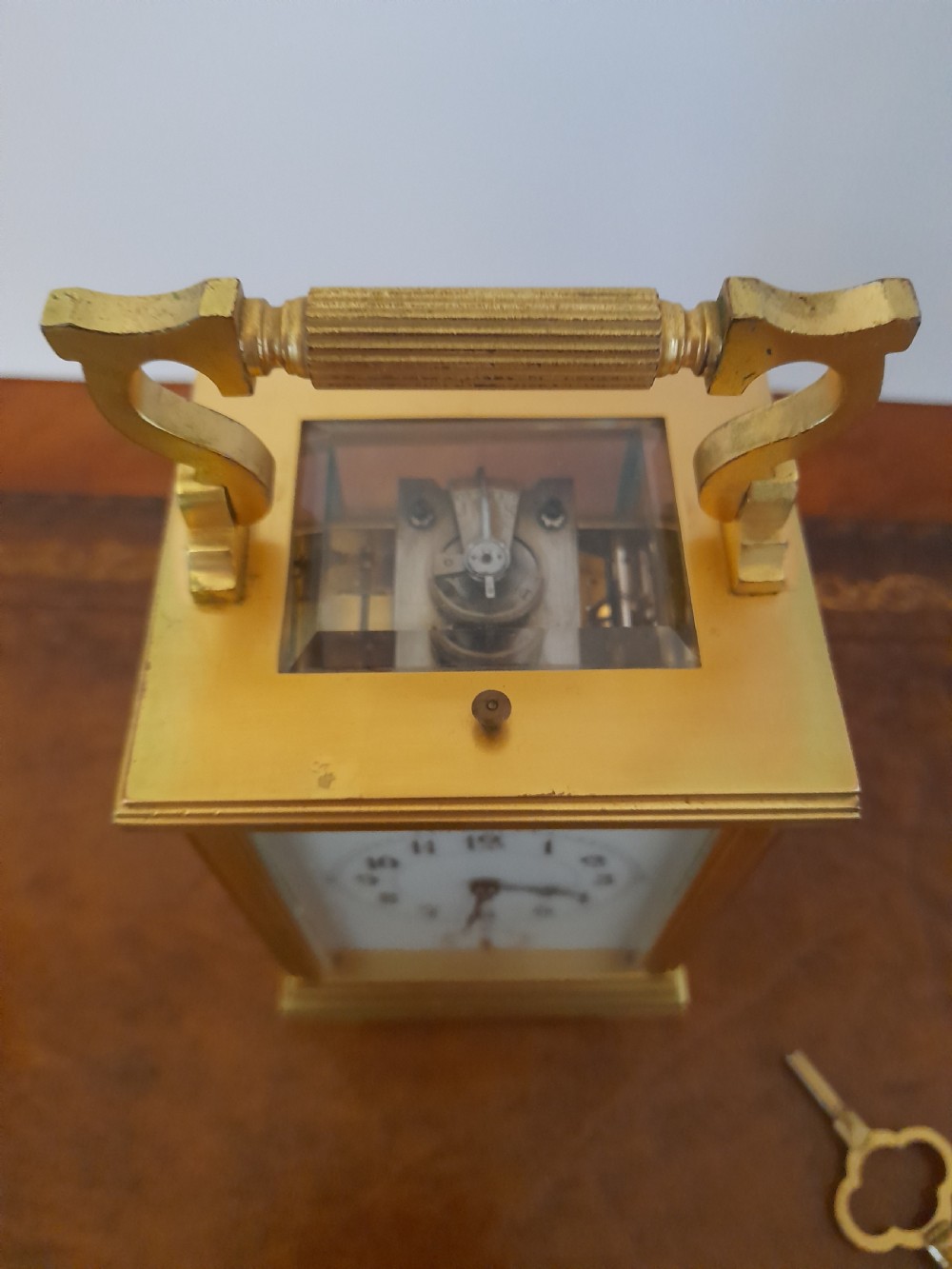 A gilt brass carriage clock featuring a fluted top handle, bevelled glass panels, a white enamel main dial with Arabic numerals, an alarm sub-dial, and an accompanying winding key. View IX