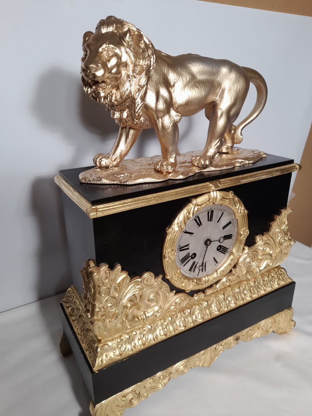 A French Empire style mantel clock featuring a gilded lion sculpture on top of a black rectangular casing adorned with gold acanthus mounts and a central clock dial. View III