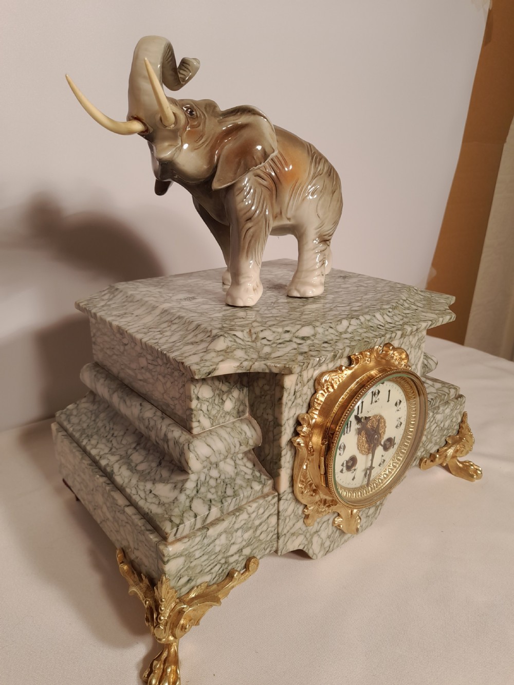 An antique mantel clock crafted from veined green marble with decorative gilt mounts and a glazed ceramic elephant figure resting on top. View II