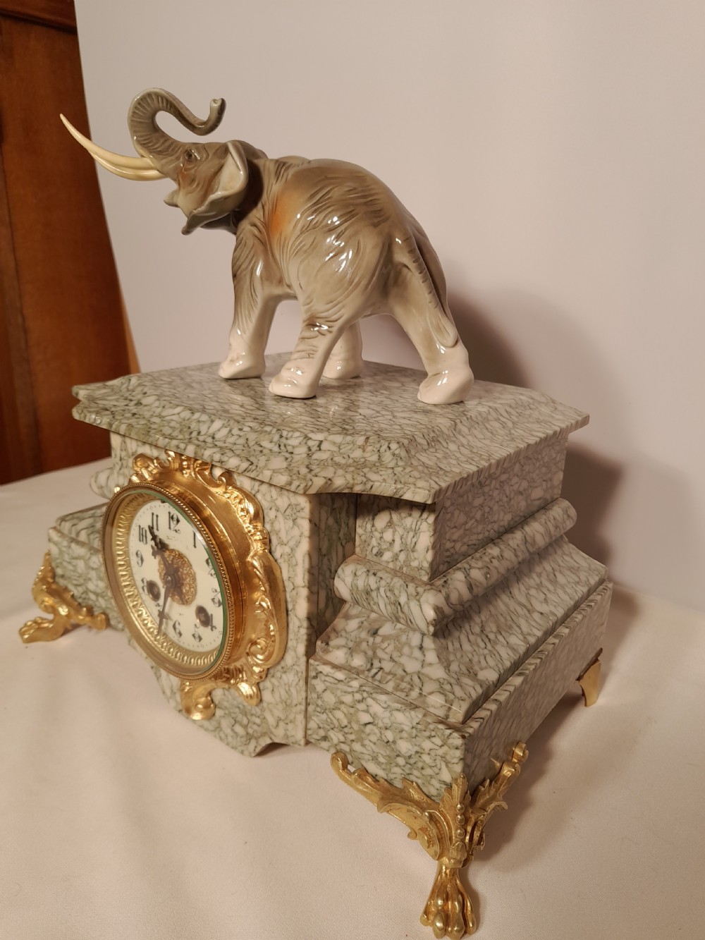 An antique mantel clock crafted from veined green marble with decorative gilt mounts and a glazed ceramic elephant figure resting on top. View III