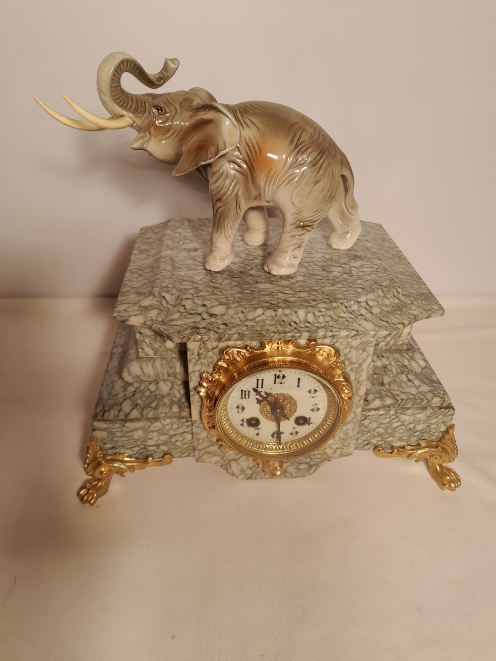 An antique mantel clock crafted from veined green marble with decorative gilt mounts and a glazed ceramic elephant figure resting on top. View V