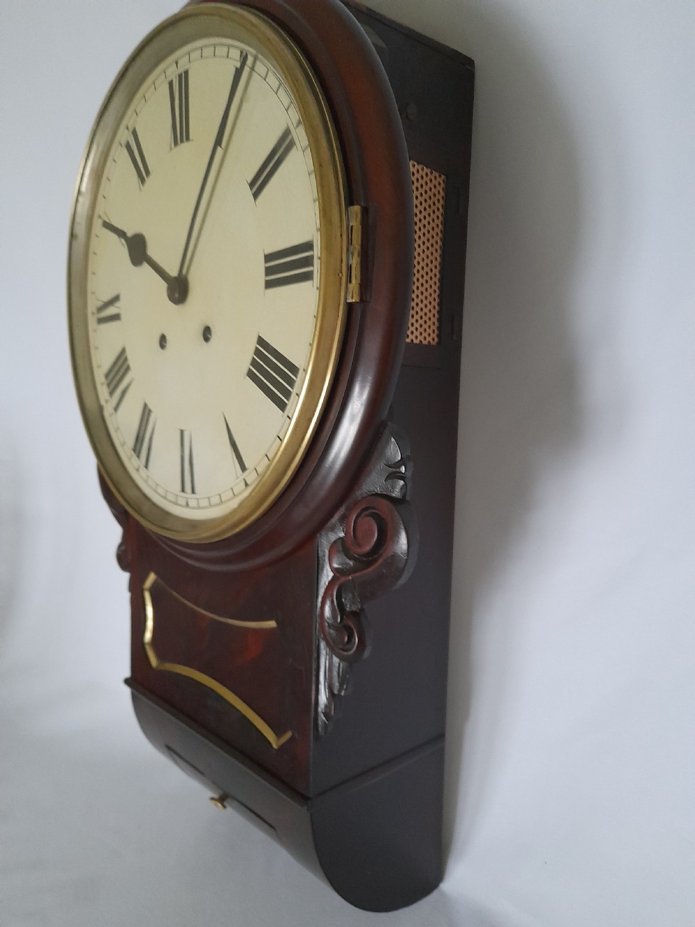An antique Victorian drop-dial wall clock crafted from polished mahogany with brass inlay detailing, carved side ears, and a circular dial featuring Roman numerals.