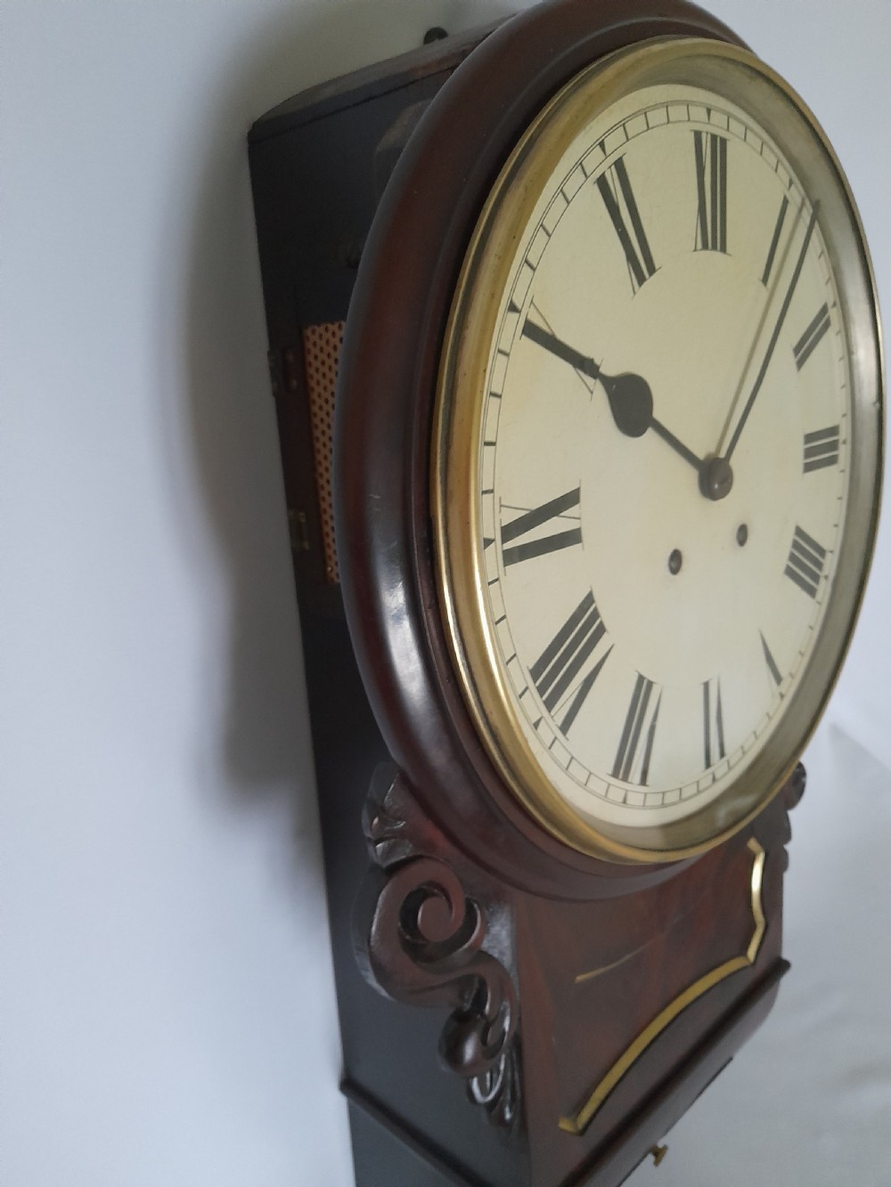 An antique Victorian drop-dial wall clock crafted from polished mahogany with brass inlay detailing, carved side ears, and a circular dial featuring Roman numerals. View II