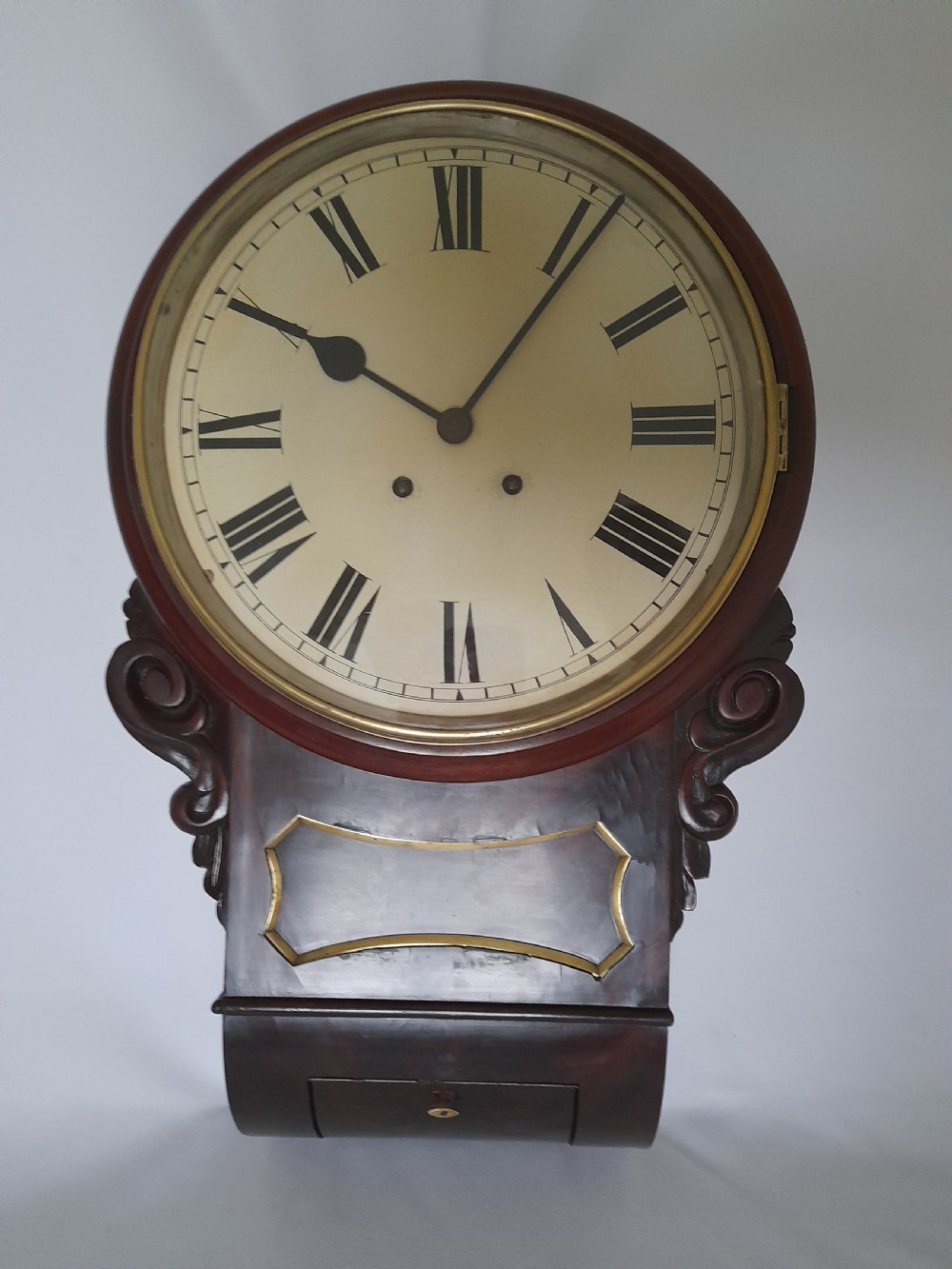 An antique Victorian drop-dial wall clock crafted from polished mahogany with brass inlay detailing, carved side ears, and a circular dial featuring Roman numerals. View III