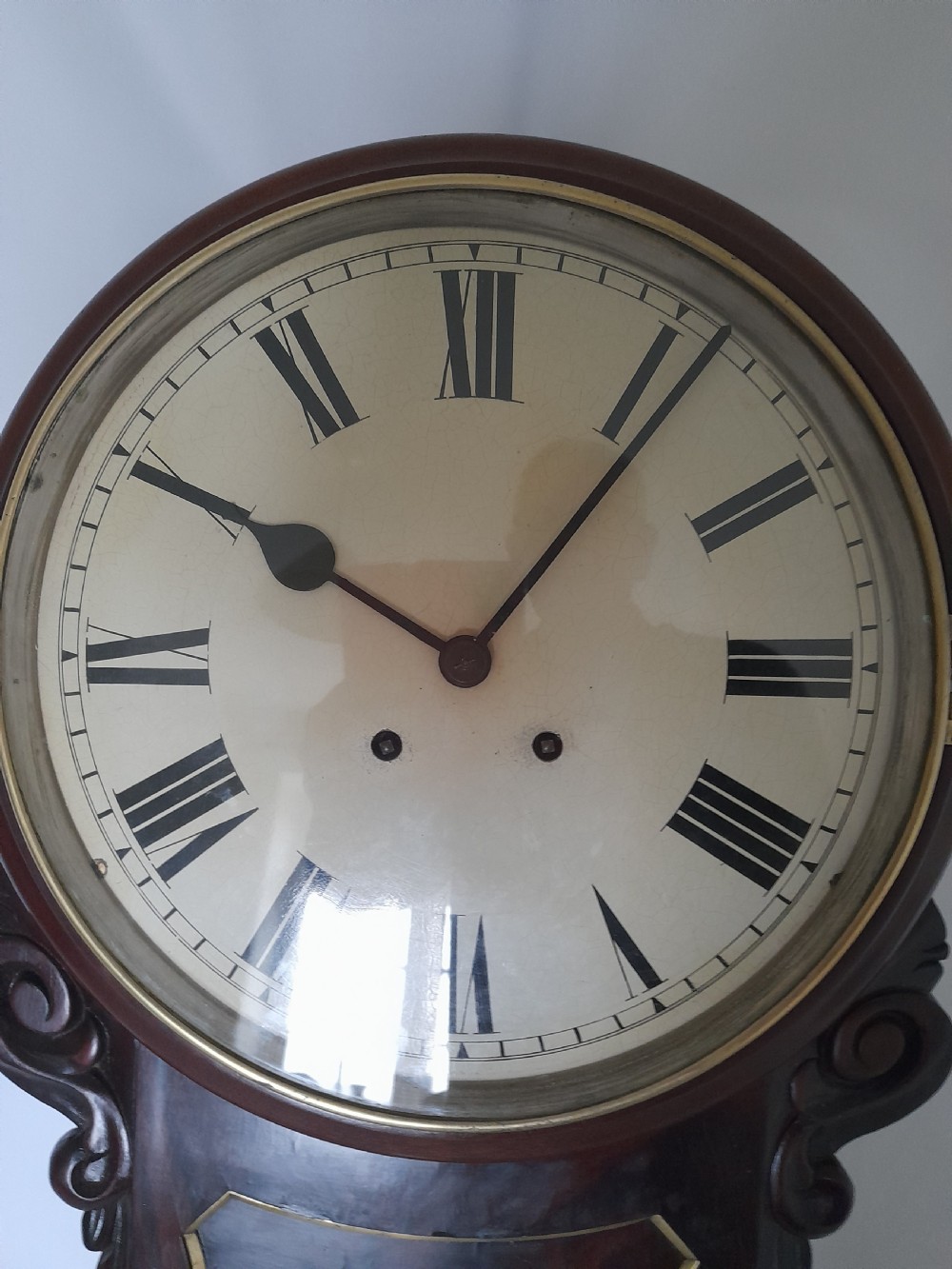 An antique Victorian drop-dial wall clock crafted from polished mahogany with brass inlay detailing, carved side ears, and a circular dial featuring Roman numerals. View V