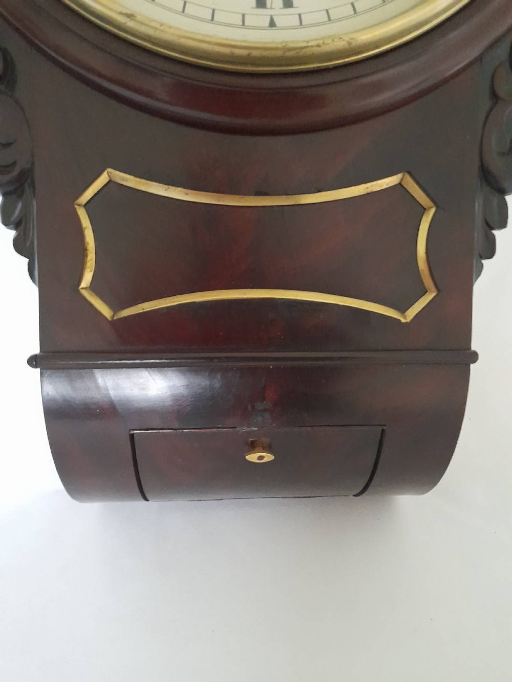 An antique Victorian drop-dial wall clock crafted from polished mahogany with brass inlay detailing, carved side ears, and a circular dial featuring Roman numerals. View VI