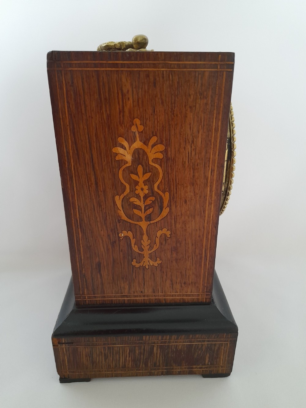 An antique French officers clock with a dark wood inlaid rectangular case, a decorative brass carrying handle, and a white enamel clock face with Roman numerals. View III