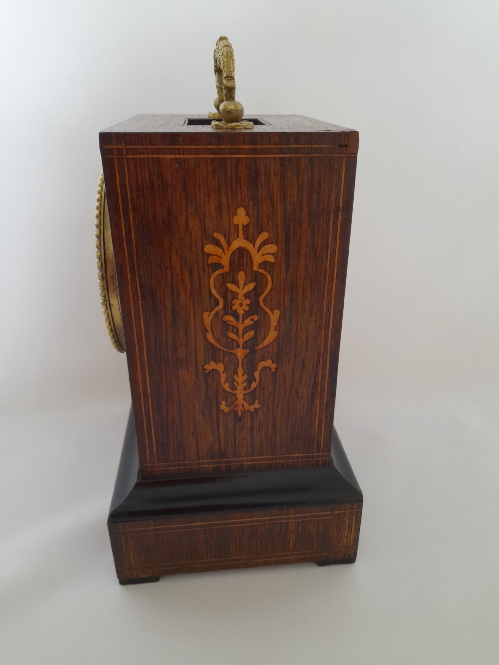 An antique French officers clock with a dark wood inlaid rectangular case, a decorative brass carrying handle, and a white enamel clock face with Roman numerals. View VI