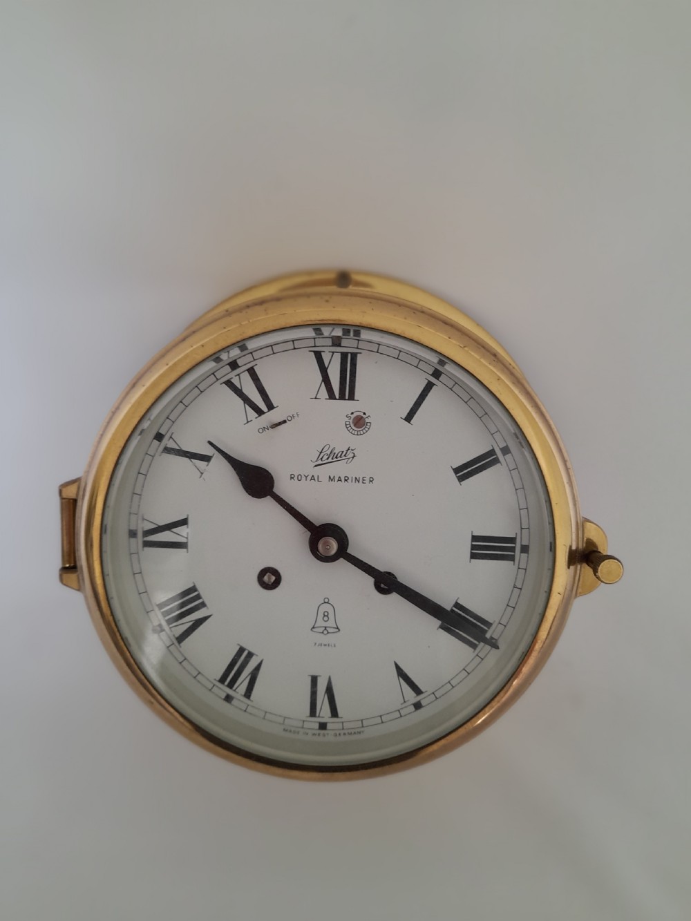A circular brass Schatz Royal Mariner maritime wall clock with a white face, black Roman numerals, and a hinged glass front.