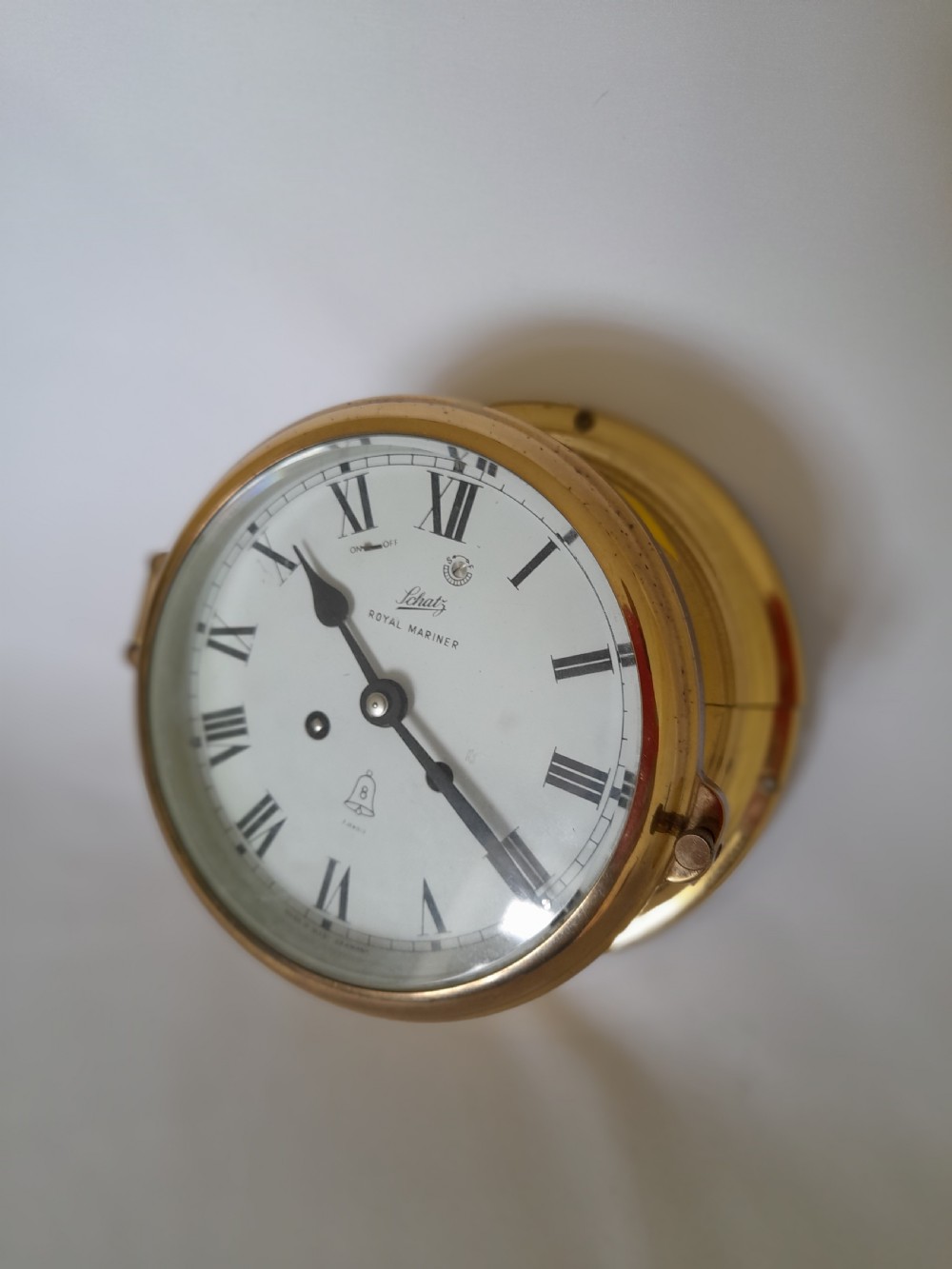 A circular brass Schatz Royal Mariner maritime wall clock with a white face, black Roman numerals, and a hinged glass front. View II