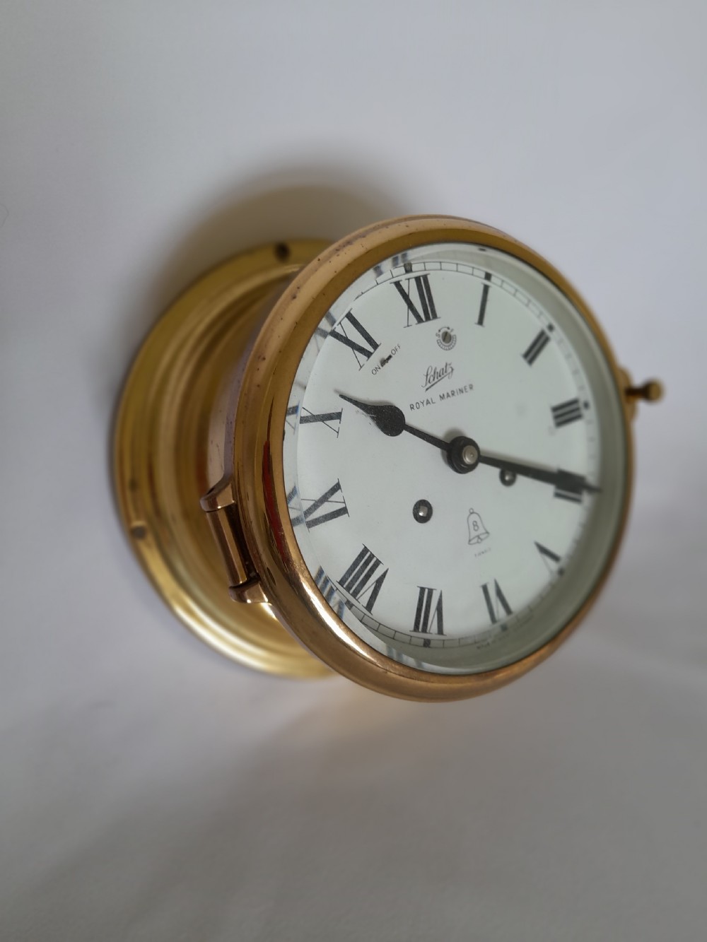 A circular brass Schatz Royal Mariner maritime wall clock with a white face, black Roman numerals, and a hinged glass front. View III