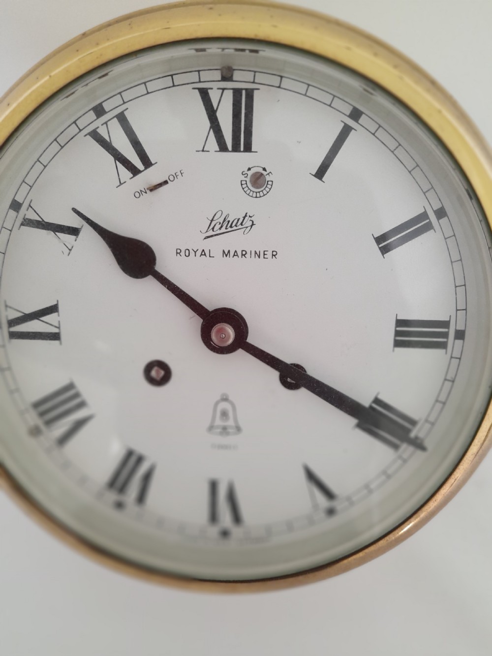A circular brass Schatz Royal Mariner maritime wall clock with a white face, black Roman numerals, and a hinged glass front. View IV